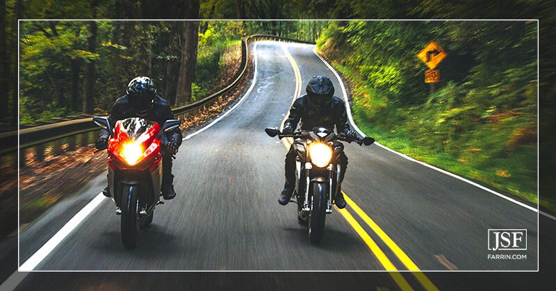 Two motorcyclists biking in the wrong lane on a narrow, winding forest road.