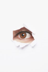 Insurance adjuster spying on you through a rip in a white canvas.