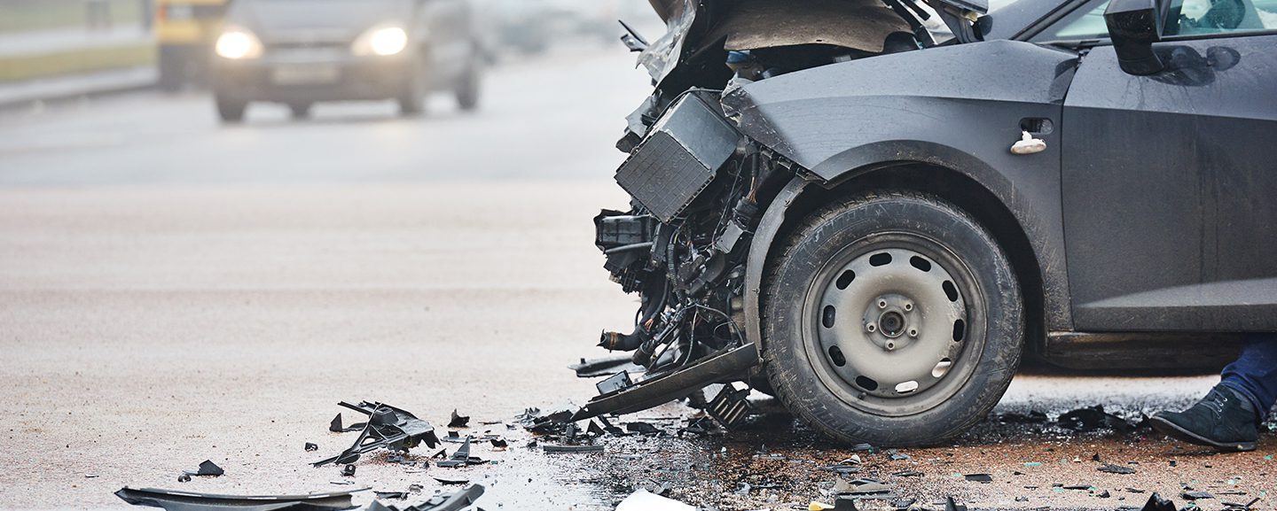 Aftermath of a car crash on a road in the rain. The front of the car is wrecked & the car is totaled.