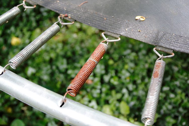 A rusted spring on an outdoor trampoline, creating a hazard.